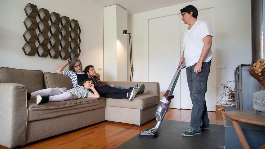 Are Cordless Vacuums Good? - Family resting in the living room while the father cleans with a cordless vacuum